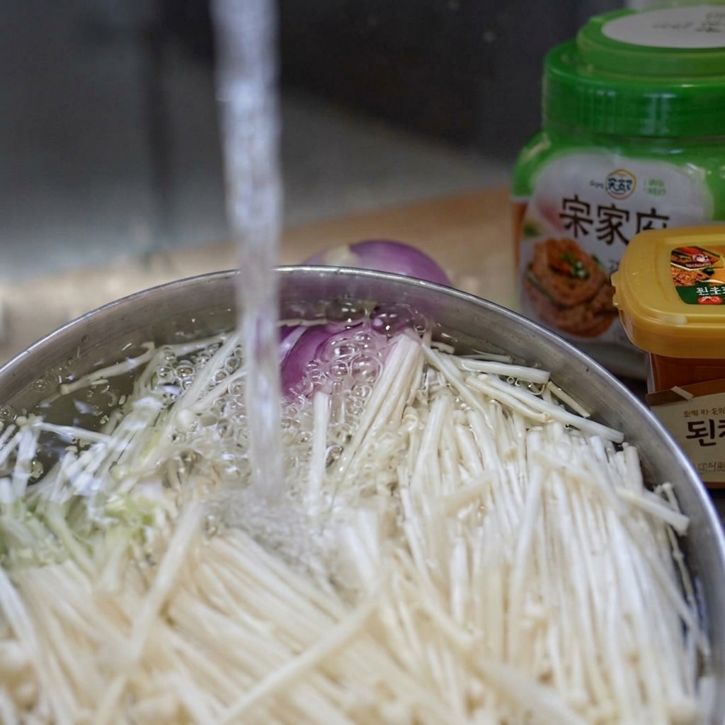 Enoki-Pilze in einer Schüssel unter fließendem kaltem Wasser reinigen.