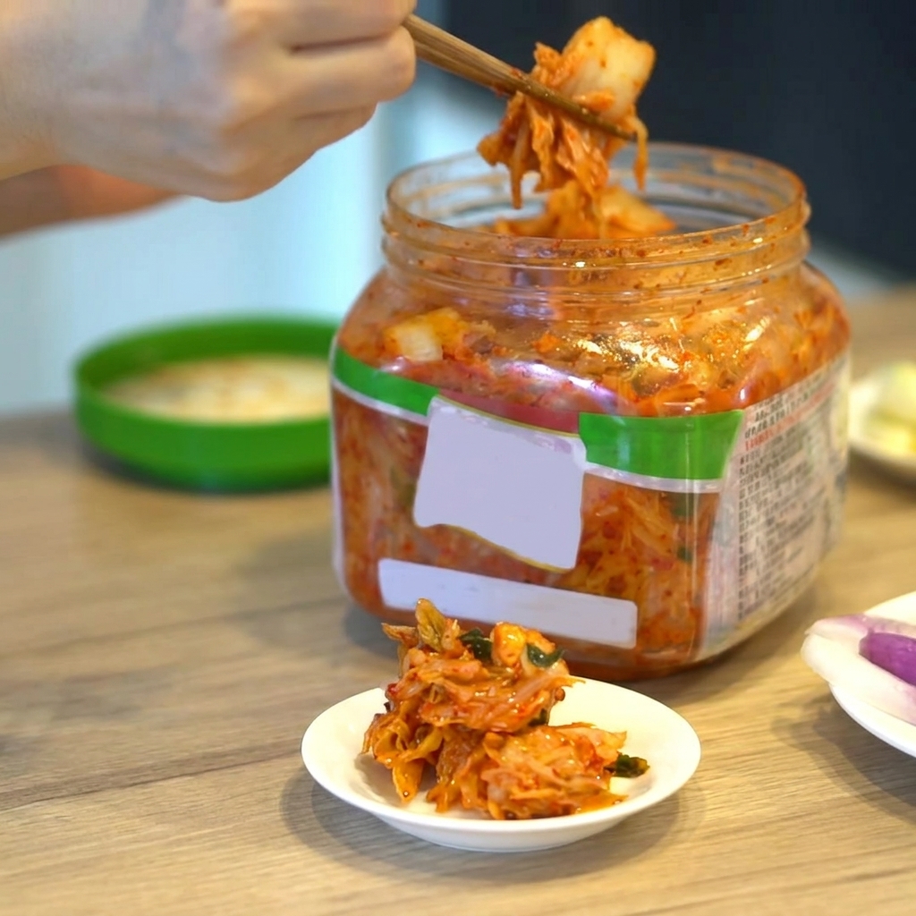 Eine Portion koreanisches Kimchi wird mit Stäbchen aus einem Behälter genommen.