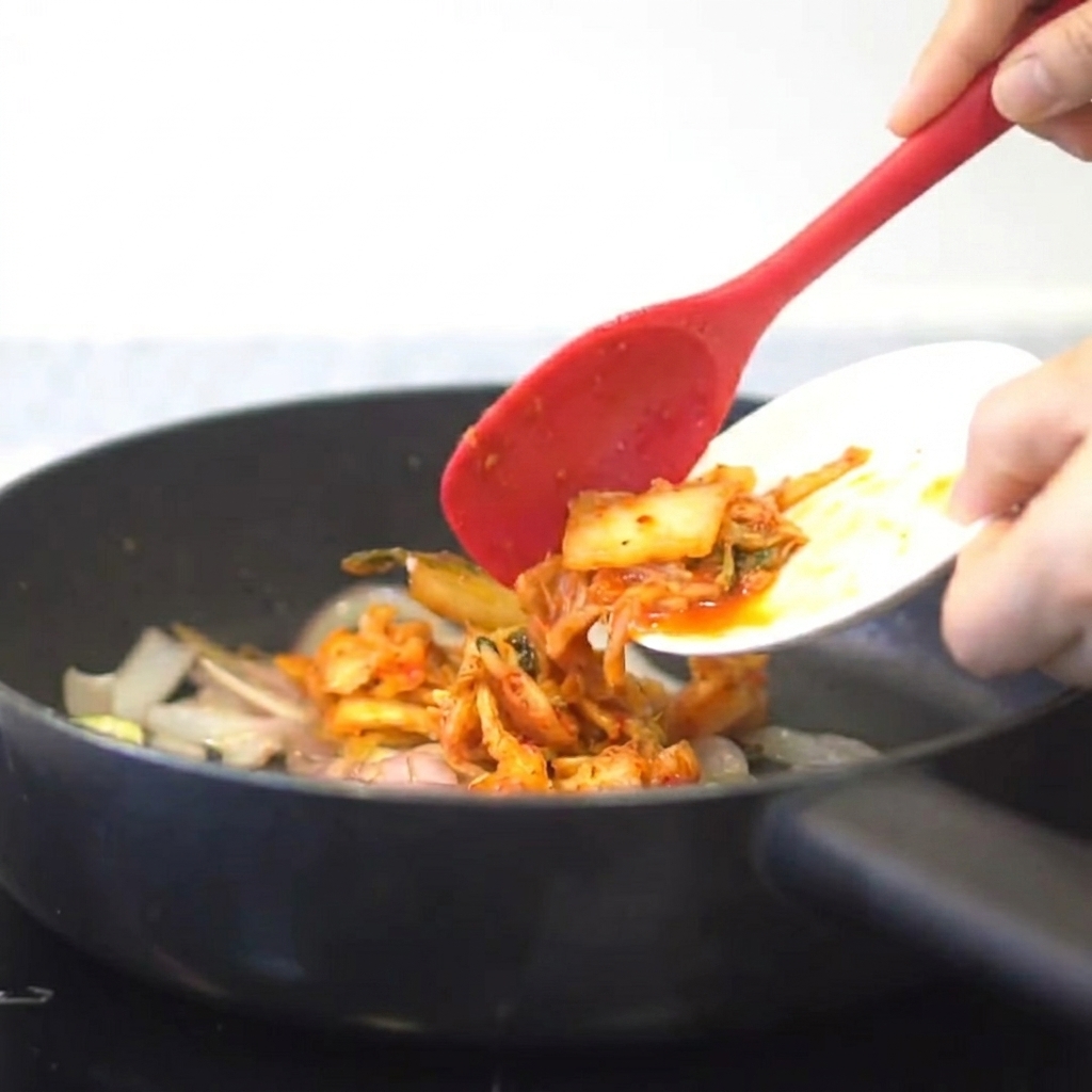 Kimchi wird zu den angebratenen Zwiebeln und dem Knoblauch in die Pfanne gegeben.
