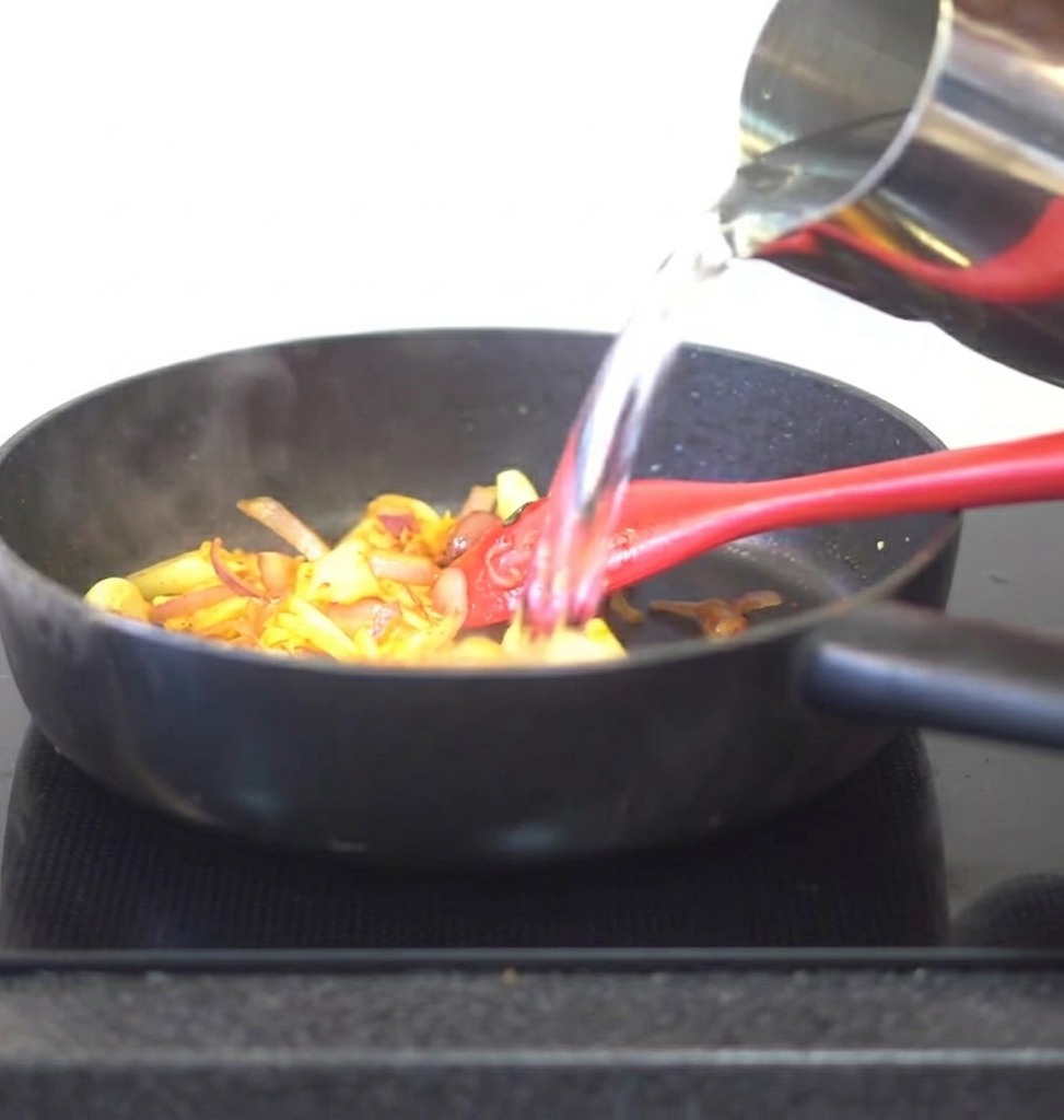 Wasser wird aus einem Metallkrug in die Pfanne mit Kimchi und Gewürzen gegossen.