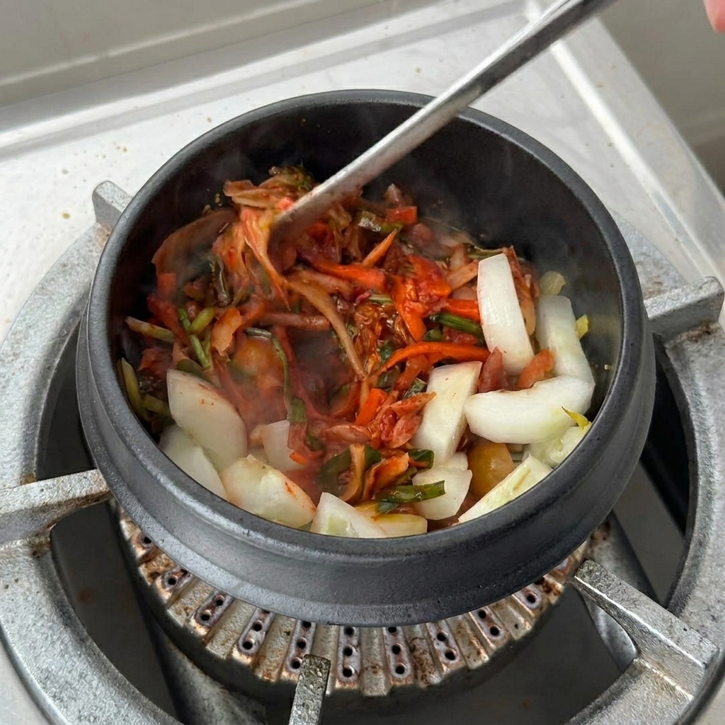 Kimchi-Lake wird über die angebratenen Zutaten in den Tontopf gegossen.