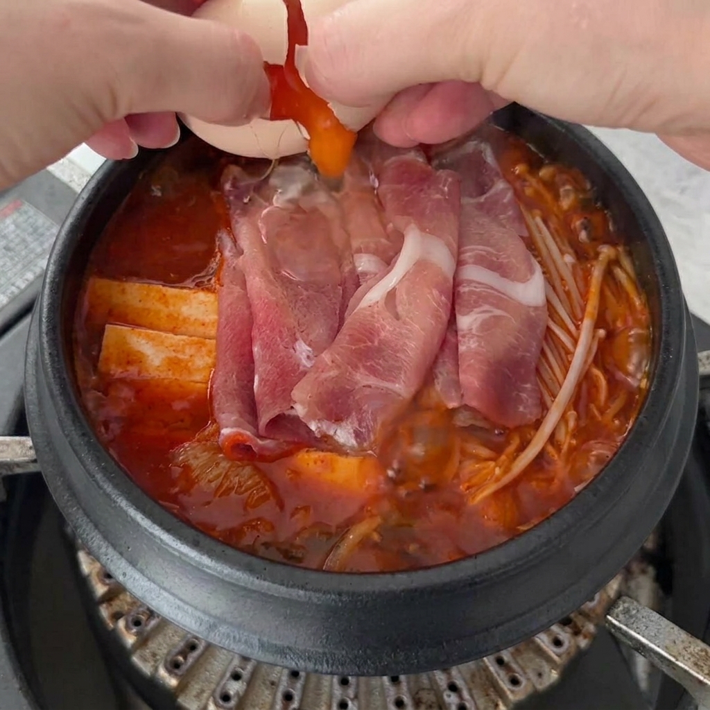 Zwei Eier werden auf die Oberfläche des sprudelnden Kimchi-Eintopfs aufgeschlagen.