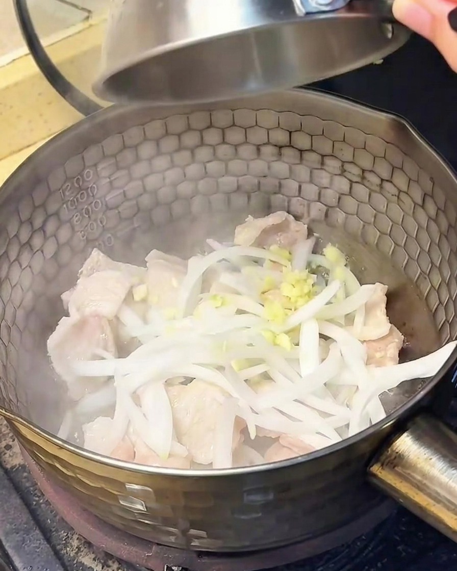 Zwiebelscheiben und gehackter Knoblauch werden in den Topf mit dem gebratenen Schweinebauch gegeben.