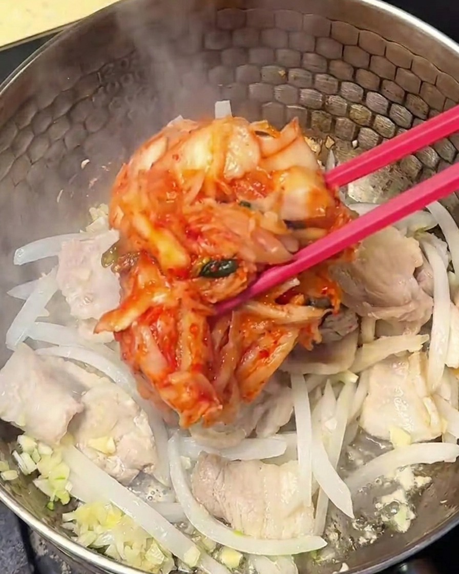Rotes, gewürztes Kimchi wird in die Schweinefleisch-Zwiebel-Mischung im Topf eingerührt.