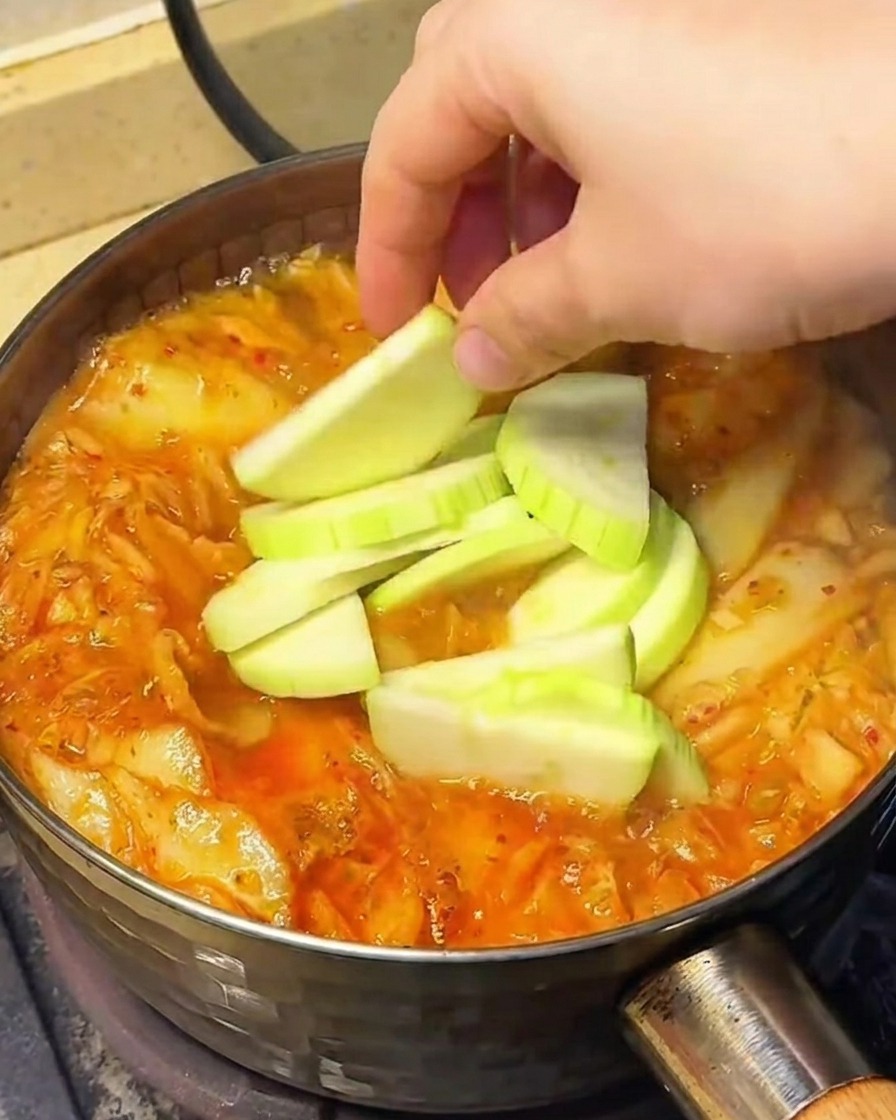Gemüse wie Chayotescheiben, Sojasprossen und Enoki-Pilze wird in die köchelnde Suppe gegeben.