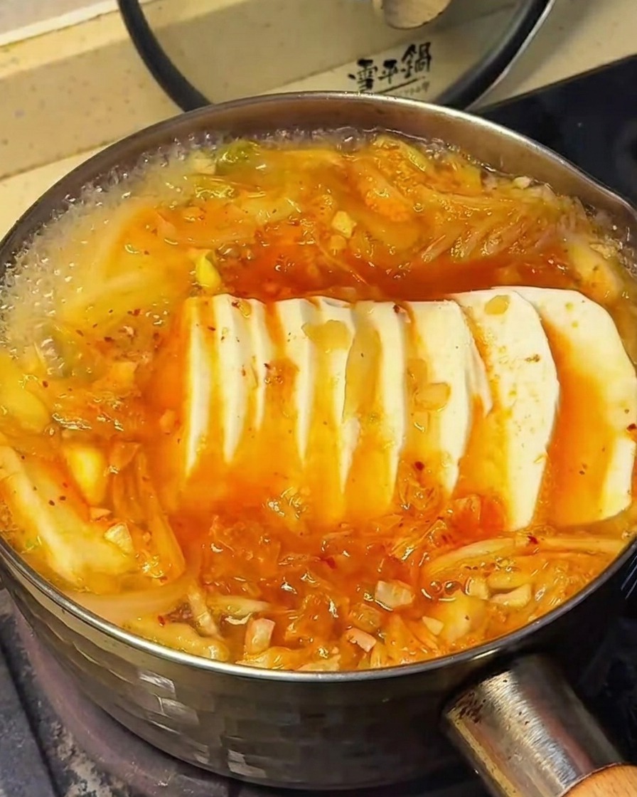 Die Oberfläche der Kimchi-Suppe mit Tofu, während Gewürze über die Zutaten gestreut werden.