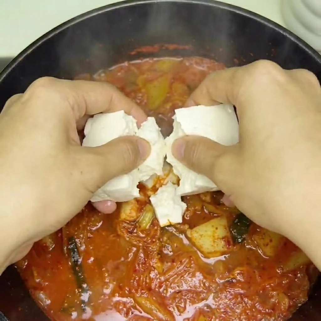 Frische Tofuwürfel werden in den köchelnden roten Kimchi-Eintopf gegeben.