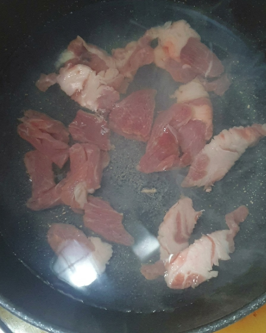 Schweinefleischstücke im Topf mit Wasser und einem Löffel gesalzenen Garnelen.
