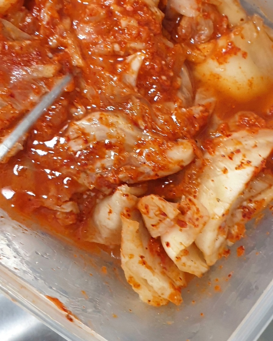 Eine Zange legt Stücke von fermentiertem Kimchi in einen brodelnden Topf.