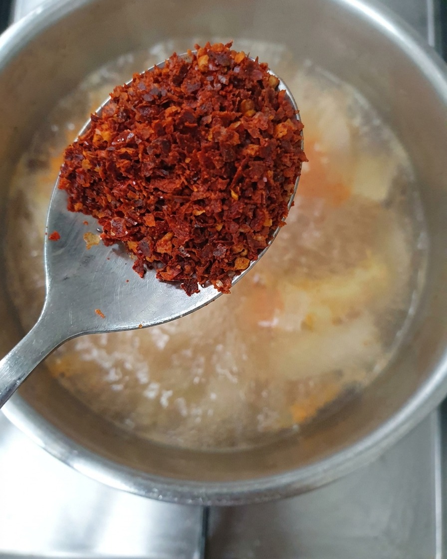 Ein Löffel mit einer Mischung aus grobem und feinem Chilipulver wird über den Eintopf gehalten.