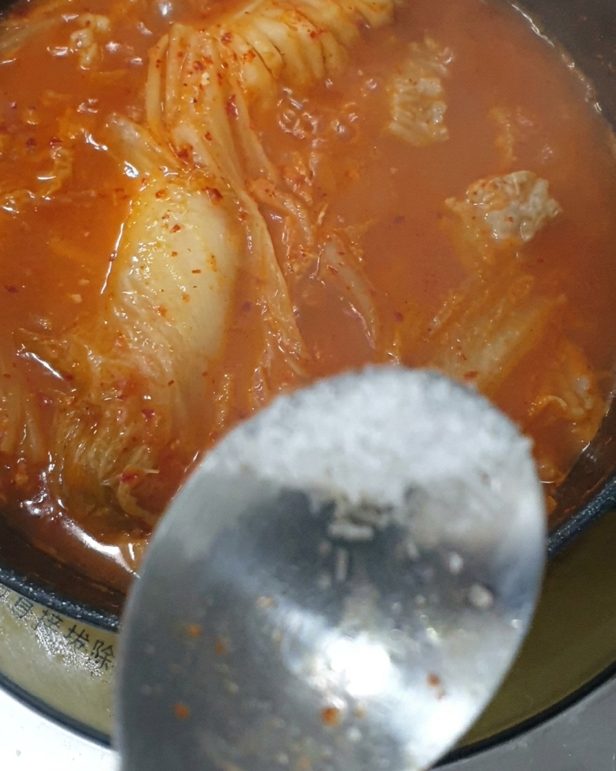 Ein Löffel Gewürz wird in den roten Kimchi-Eintopf gegeben.