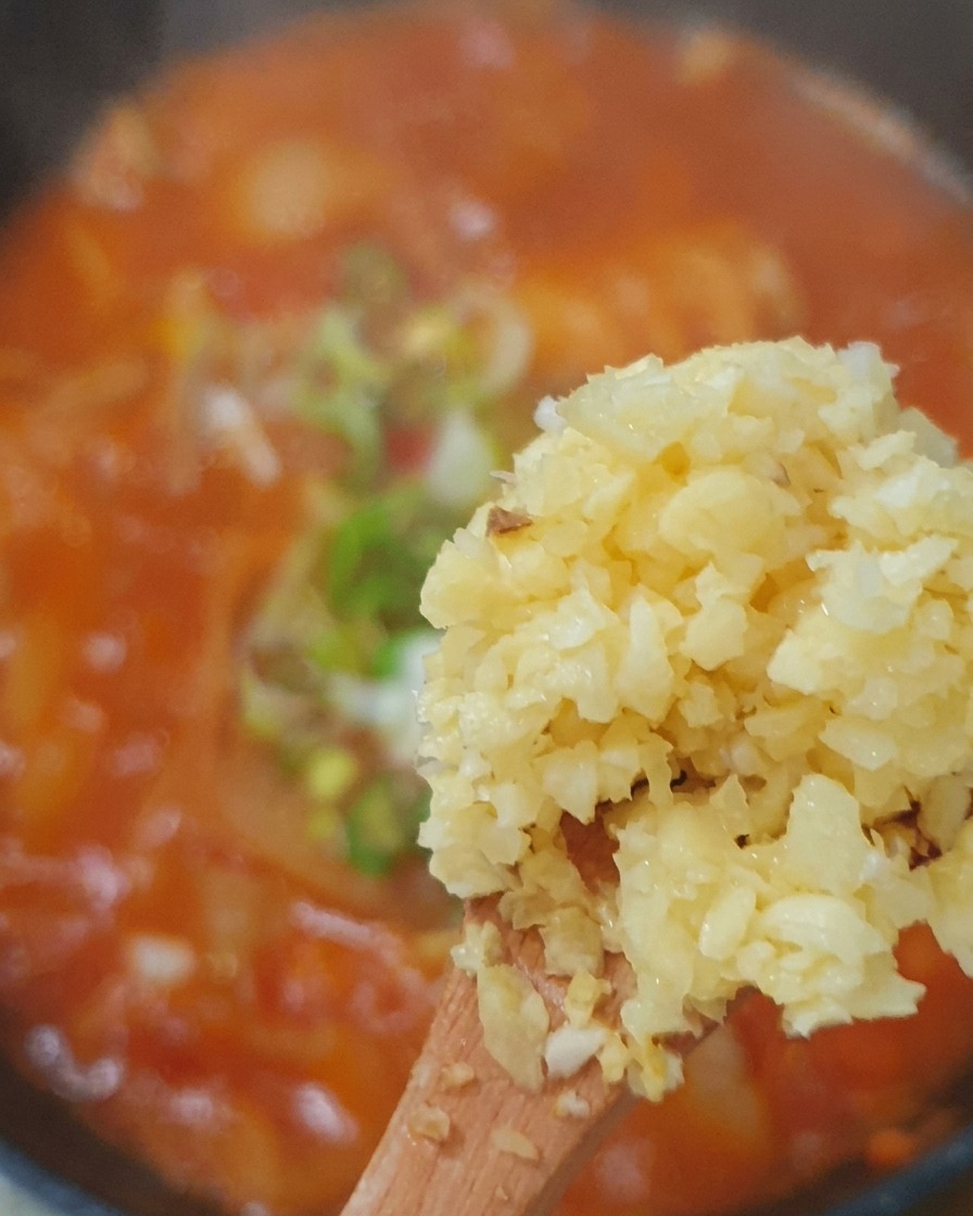 Gehackter Knoblauch, Frühlingszwiebeln und Chilischeiben werden in die Brühe gegeben.