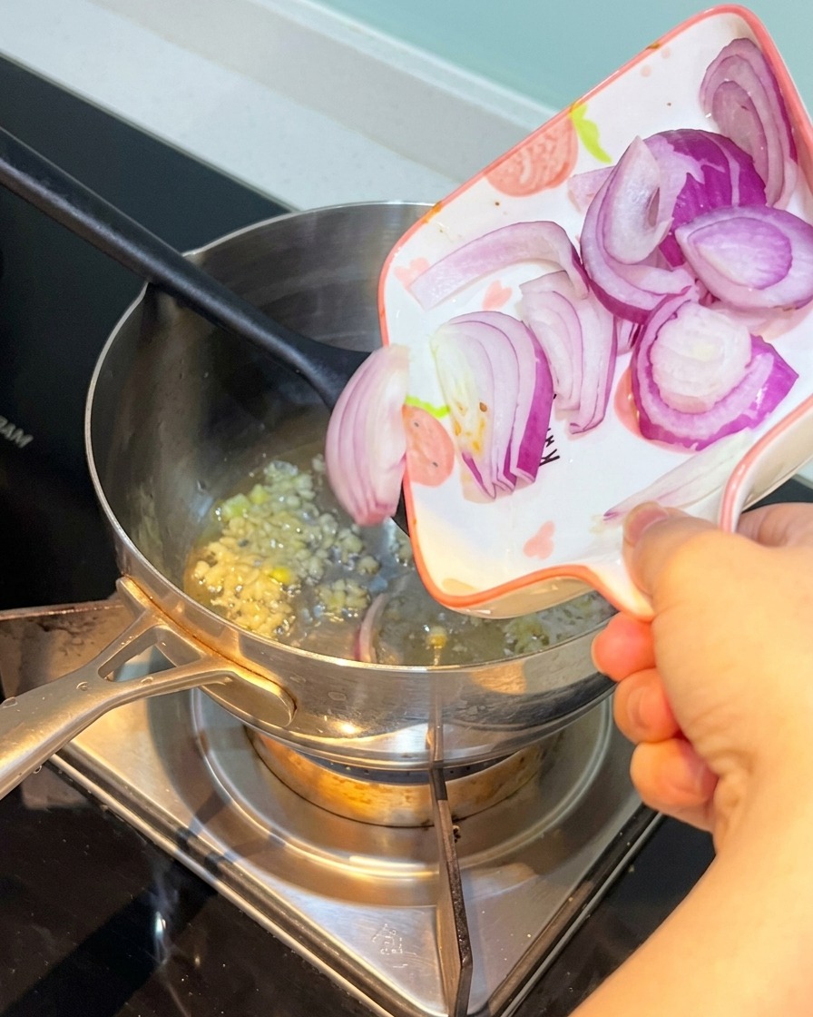 Geschnittene rote Zwiebel wird mit dem Knoblauch in den Topf gegeben.