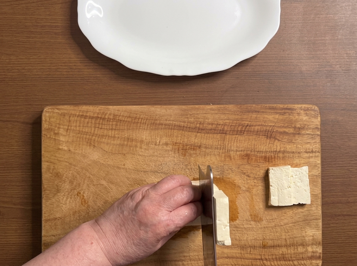 Ein Tofublock wird in dicke, saubere Scheiben auf einem Holzschneidebrett geschnitten.