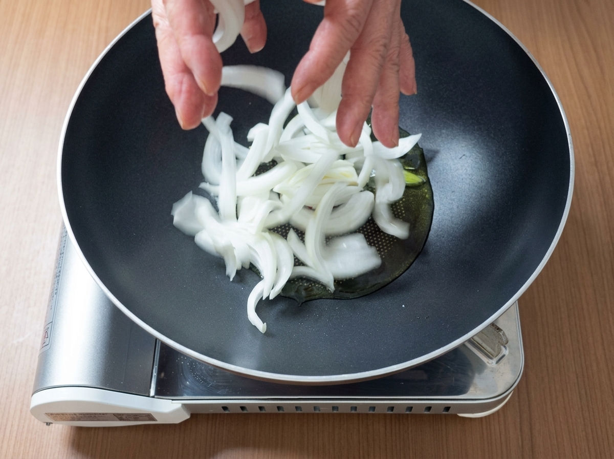 Fleischstücke und Zwiebelscheiben brutzeln zusammen mit Öl in einer Pfanne.