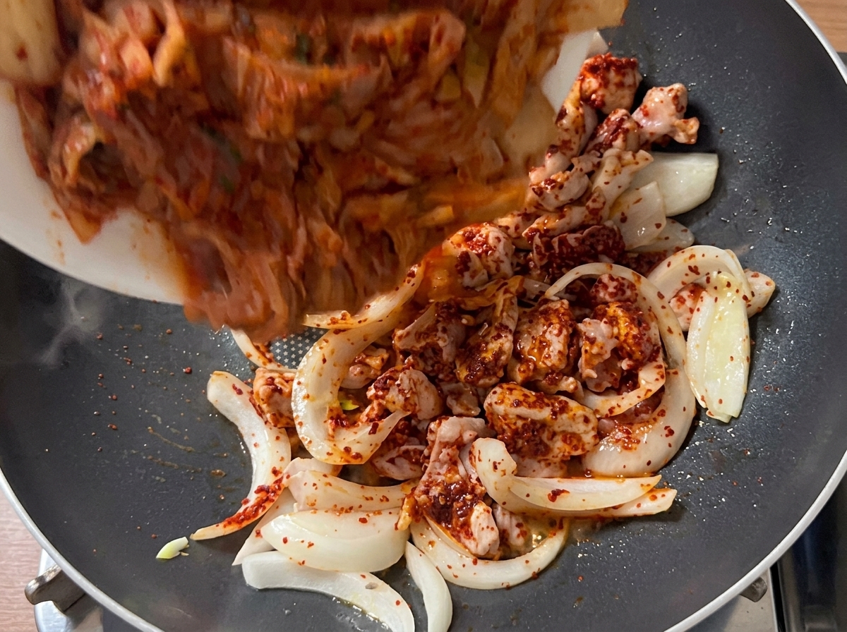 Mundgerechte Kimchistücke werden in die Pfanne zur angebratenen Fleisch-Zwiebel-Mischung gegeben.