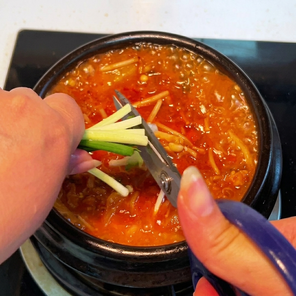 Frische Frühlingszwiebeln werden mit einer Küchenschere direkt über dem köchelnden Topf mit Kimchi-Eintopf geschnitten.