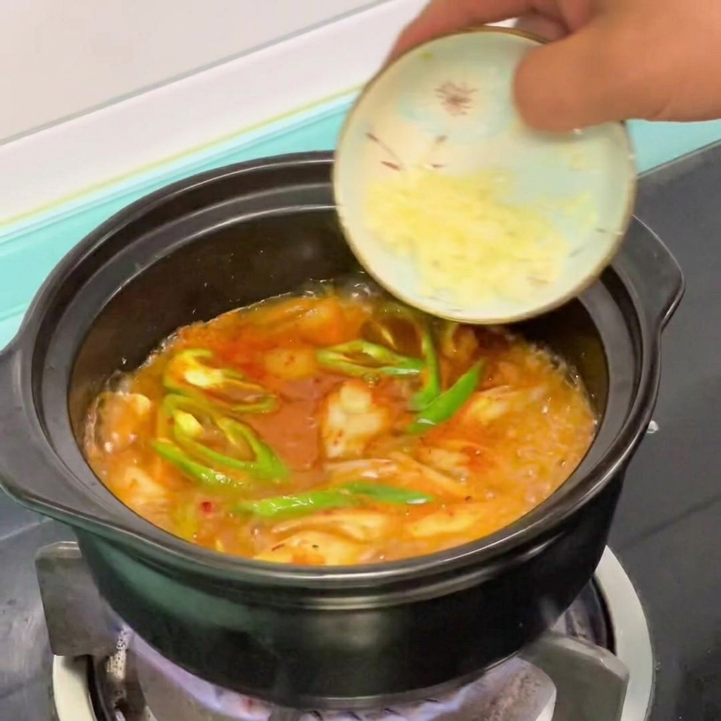 Gehackter Knoblauch wird in den köchelnden Soft-Tofu-Eintopf gegeben.