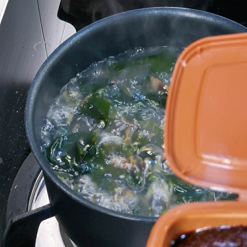 Ein Löffel braune koreanische Sojabohnenpaste wird in die kochende Suppe gerührt.