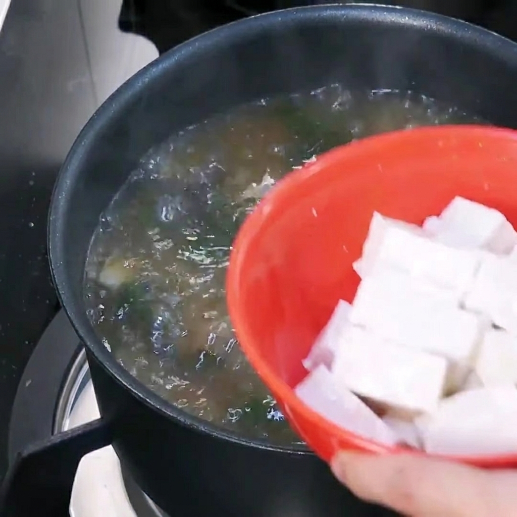 Tofuwürfel werden in die kochende Suppe gegeben.