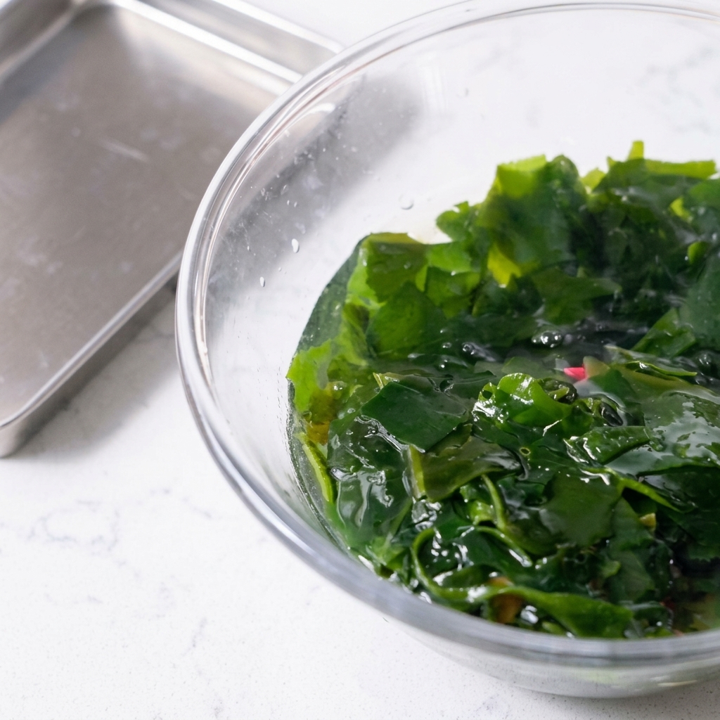 Rehydrierte Wakame-Algen werden mit einem rosa Schaumlöffel aus einer Schale gehoben.