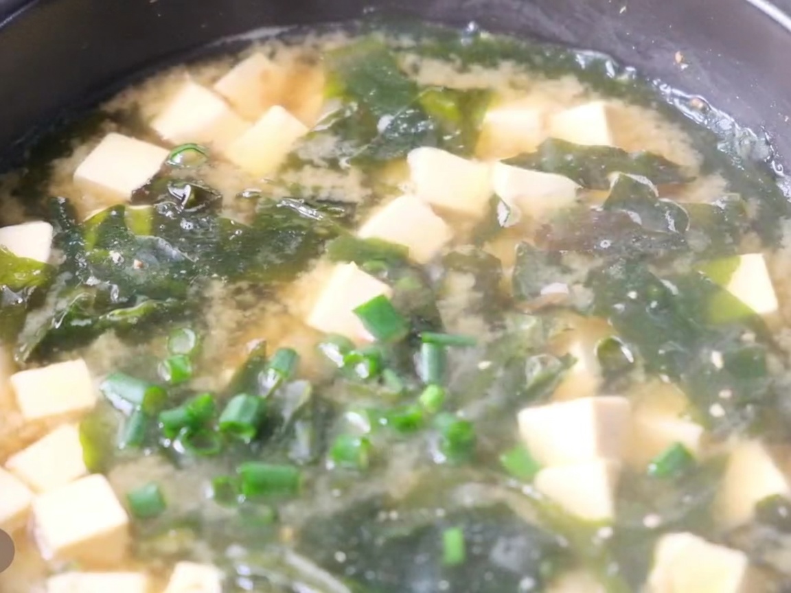Nahaufnahme eines Topfes mit heißer Miso-Suppe, Tofuwürfeln, Algen und frischen Frühlingszwiebeln.