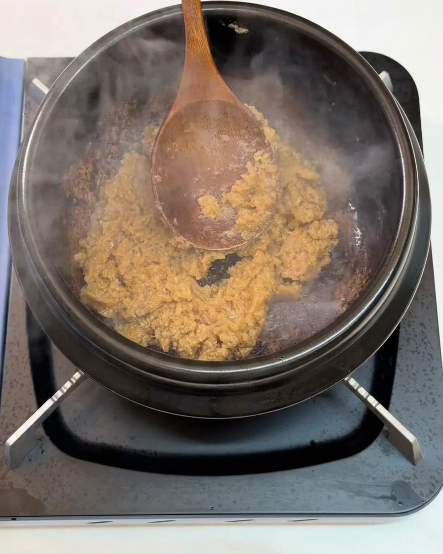Gehackter Knoblauch wird in die anbratende Sojabohnenpaste gerührt.