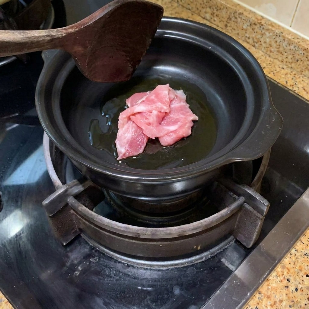 Schweinefleischscheiben werden in einem heißen Tontopf mit Öl angebraten.