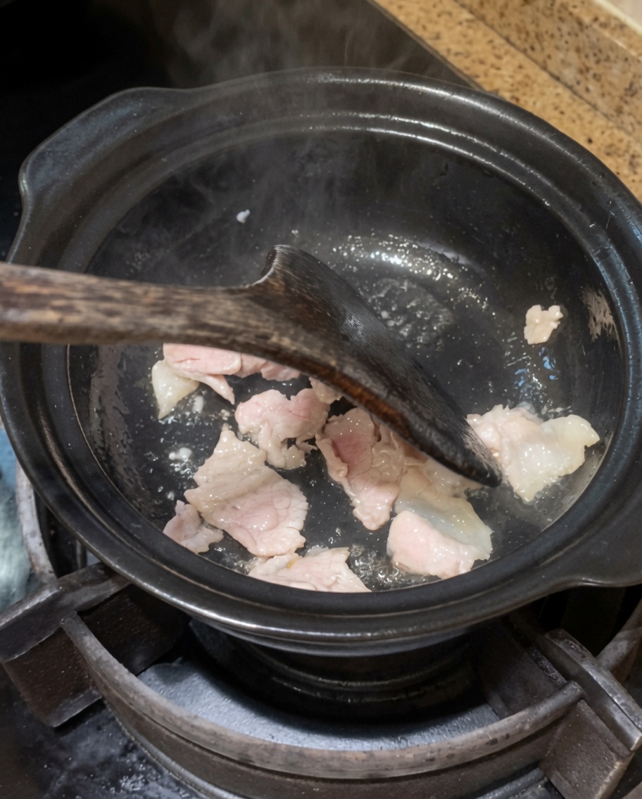 Zwiebeln und Knoblauch werden im Topf mit dem Fleisch angebraten.