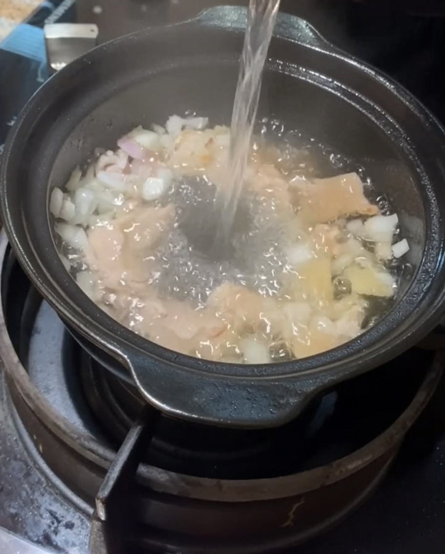 Wasser wird in den Tontopf mit Fleisch und Aromen gegossen.