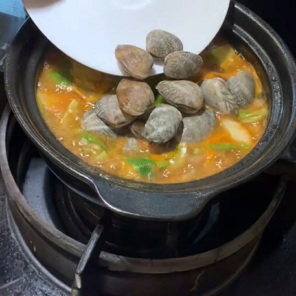 Frische Muscheln und Tofuwürfel werden vorsichtig in den sprudelnden Eintopf gegeben.