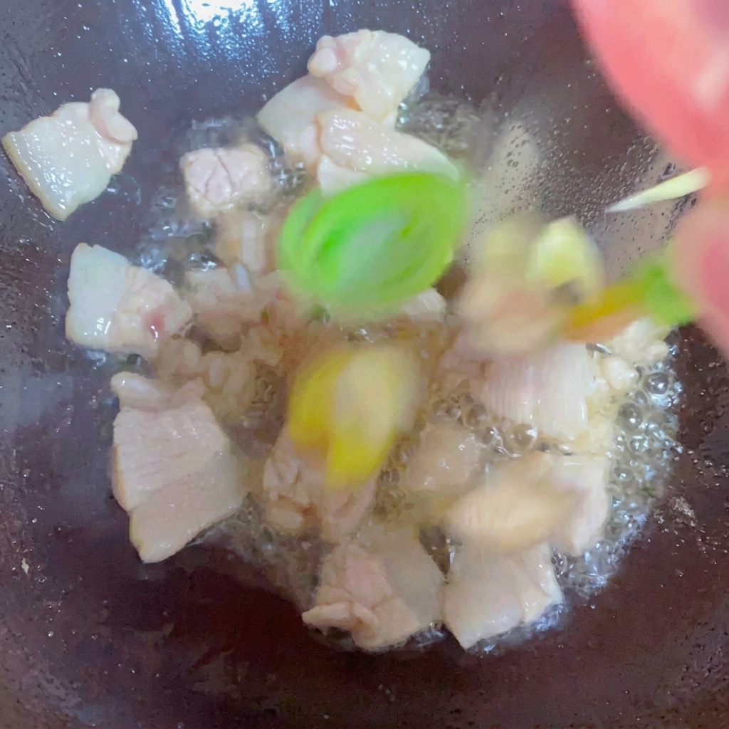 Frühlingszwiebeln, Ingwer und Knoblauch werden mit Schweinebauch im Wok angebraten.