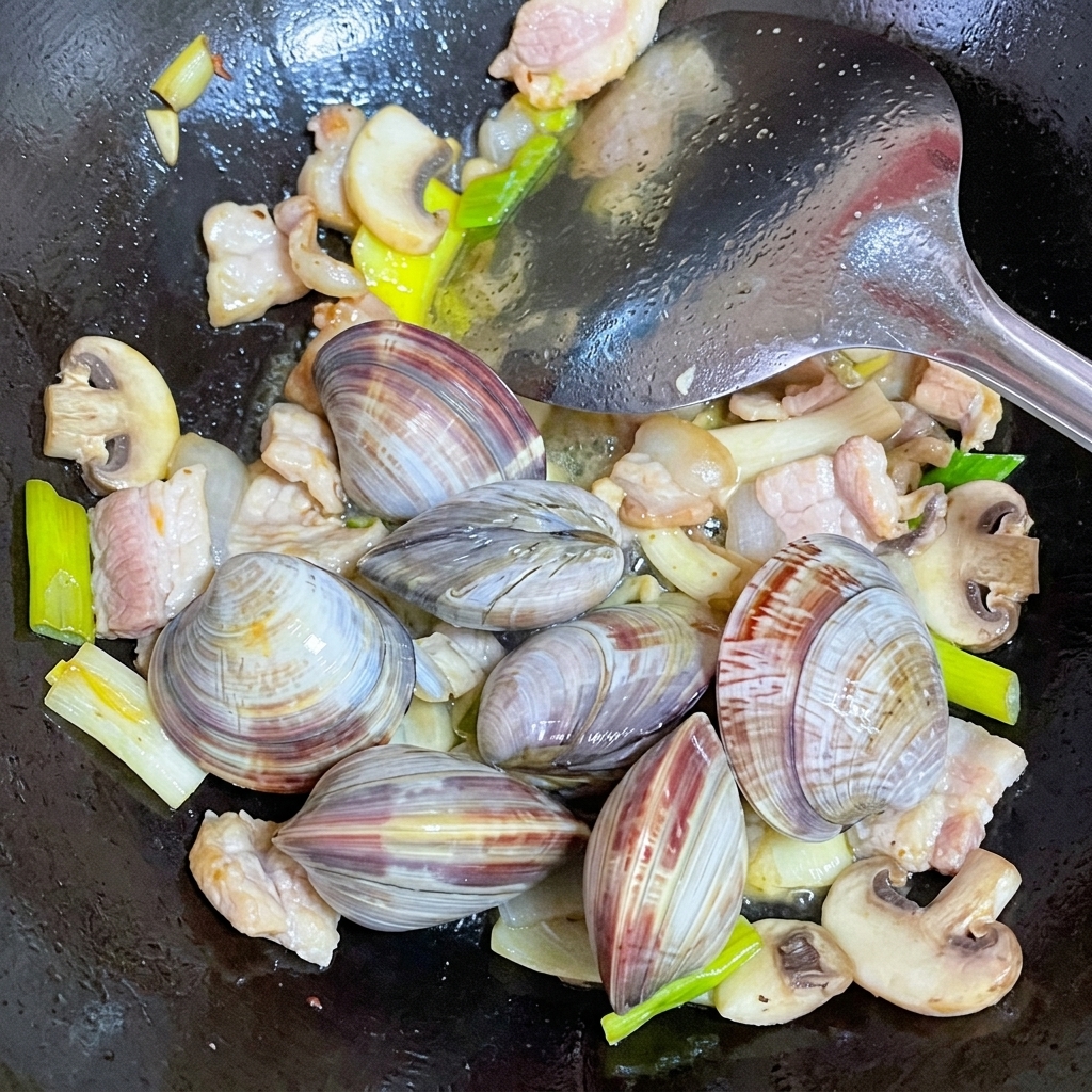 Frisch gesäuberte Muscheln werden in den Wok zu Schweinefleisch und Pilzen gegeben.