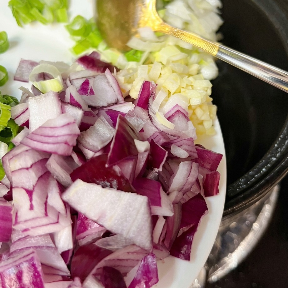 Frühlingszwiebeln, Knoblauch und rote Zwiebel werden zum gebratenen Fleisch in den Topf gegeben.