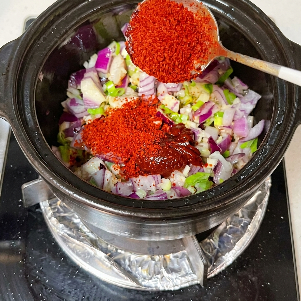 Sojasauce und Kimchi werden in den Topf zu den Zwiebeln und Aromaten gerührt.