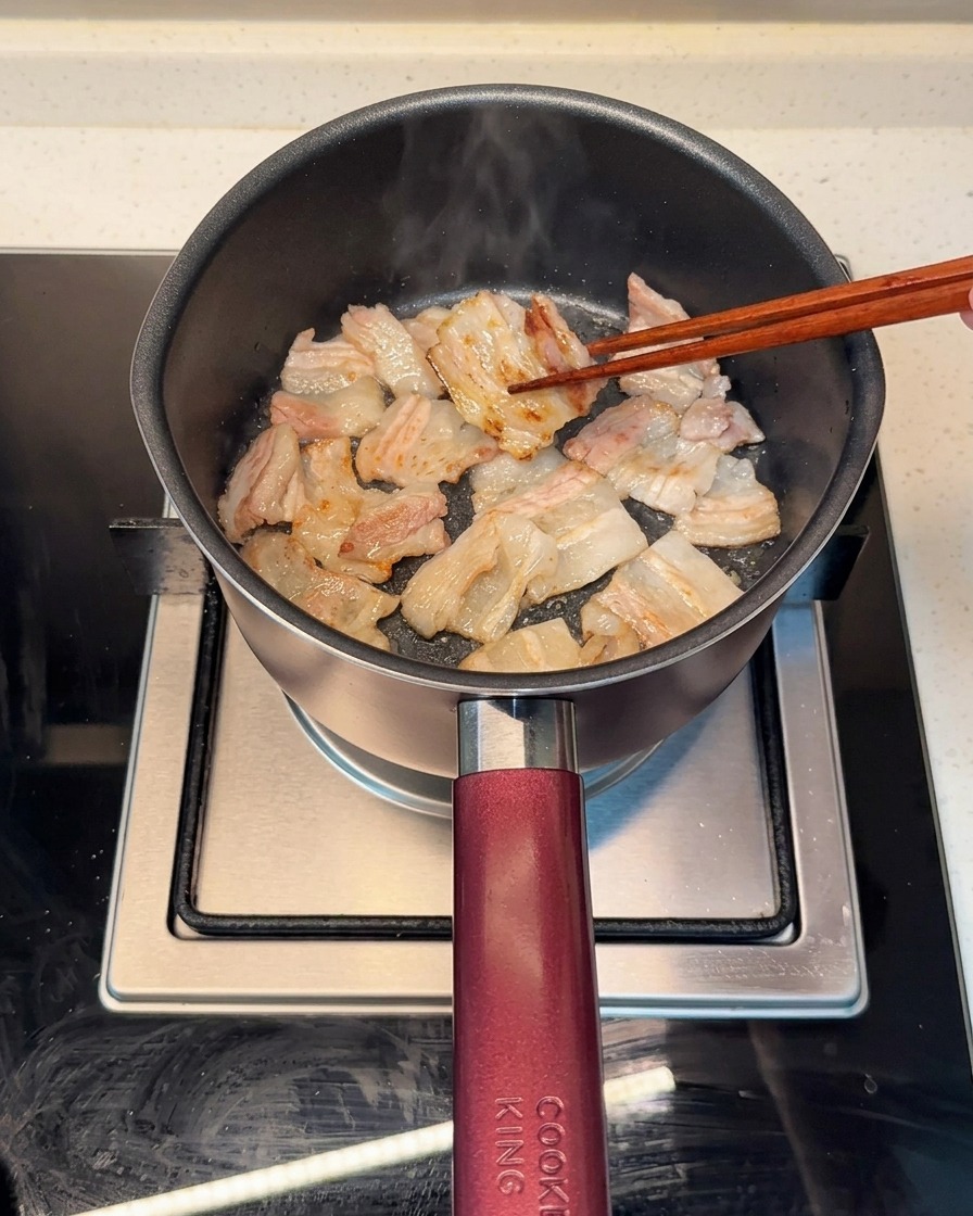 Schweinebauchscheiben bräunen gleichmäßig in einem heißen Topf, das ausgetretene Fett ist sichtbar.
