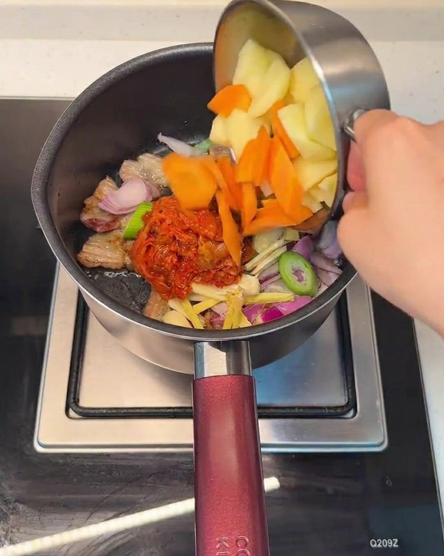 Gehackte Karotten und Kartoffeln werden in den Topf zur Kimchi-Fleisch-Mischung gegeben.