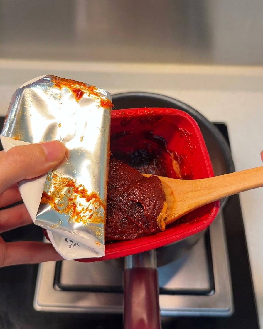 Ein Löffel rote koreanische Chilipaste wird in den Topf gegeben.