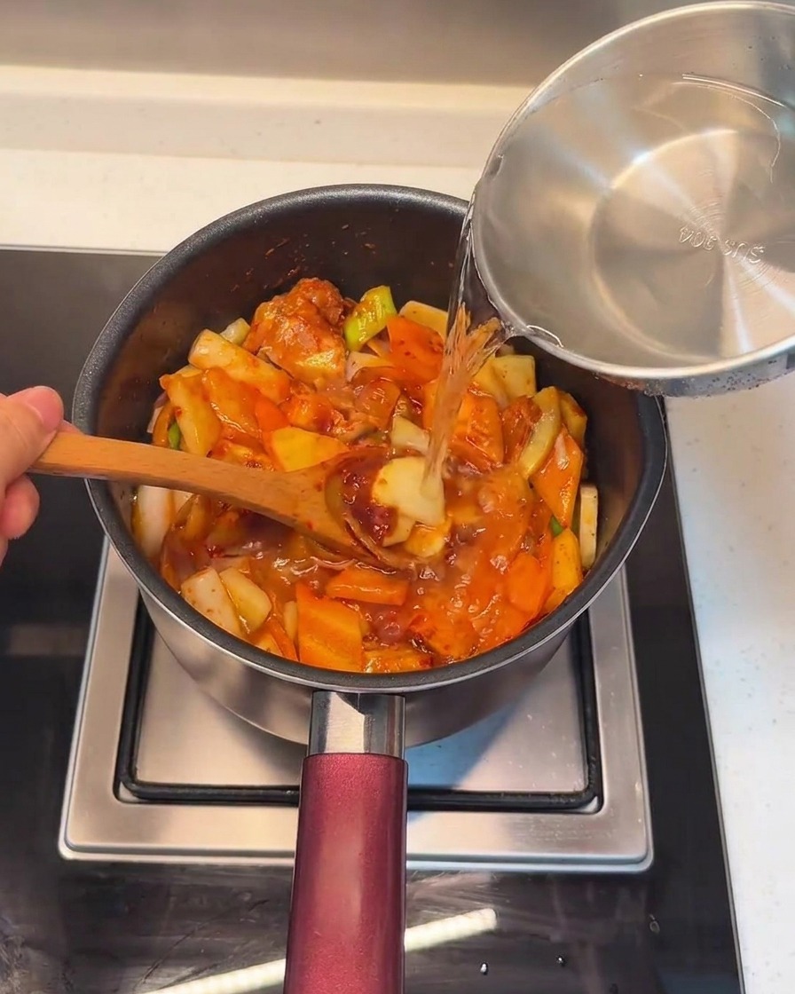 Frisches Wasser wird über die Fleisch-Gemüse-Mischung in den Topf gegossen.