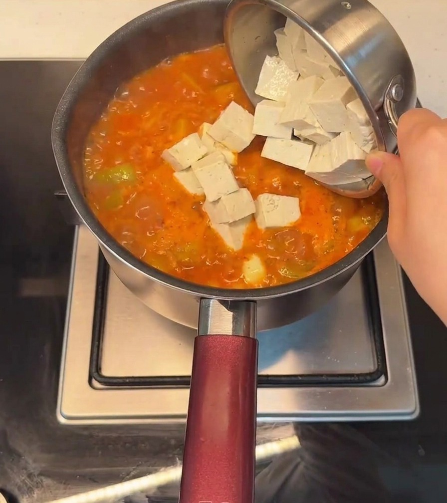Tofu-Würfel werden in den köchelnden, roten Eintopf gegeben.