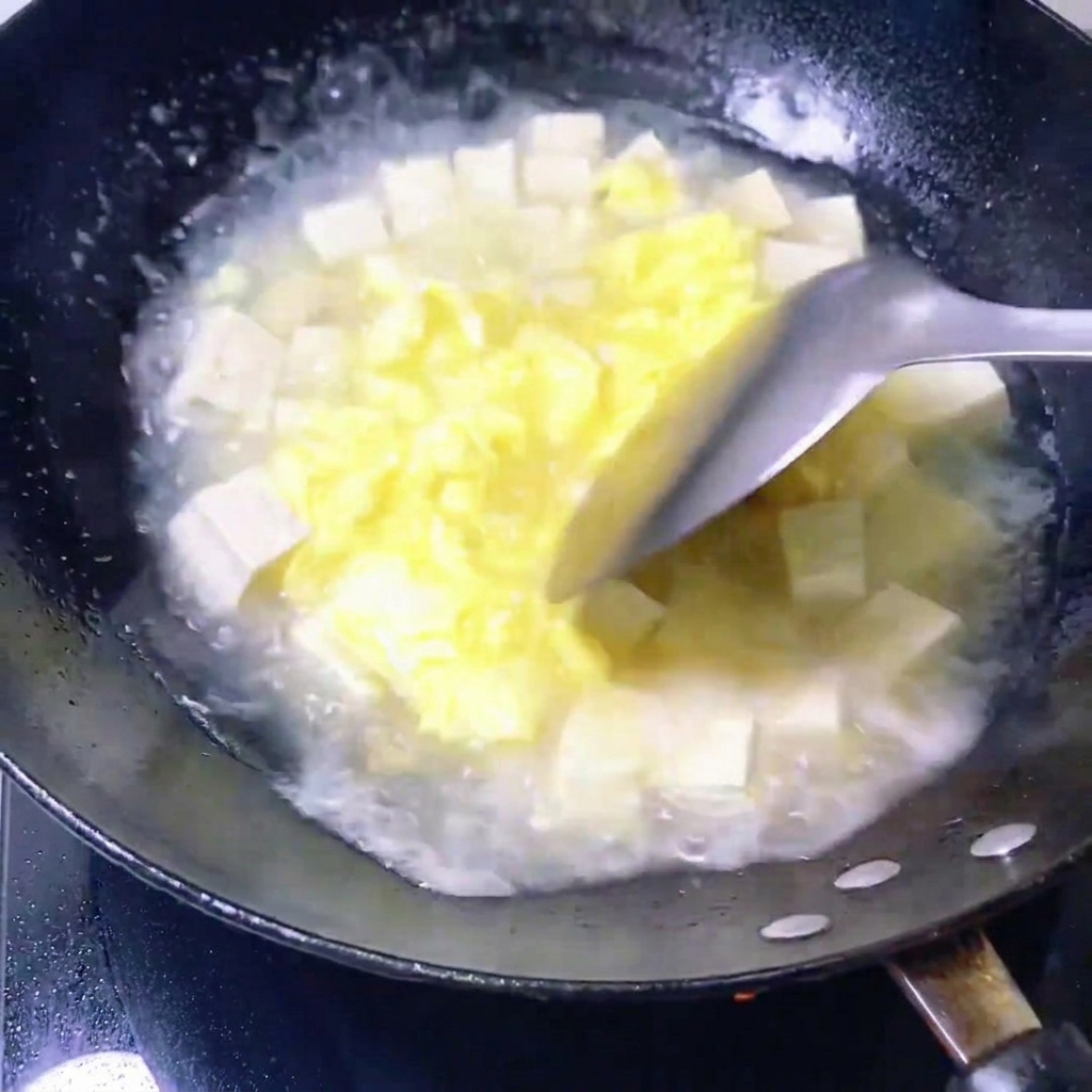 Frische Muscheln werden in eine Pfanne mit einer köchelnden Mischung aus Eierbrühe und Tofuwürfeln gegeben.