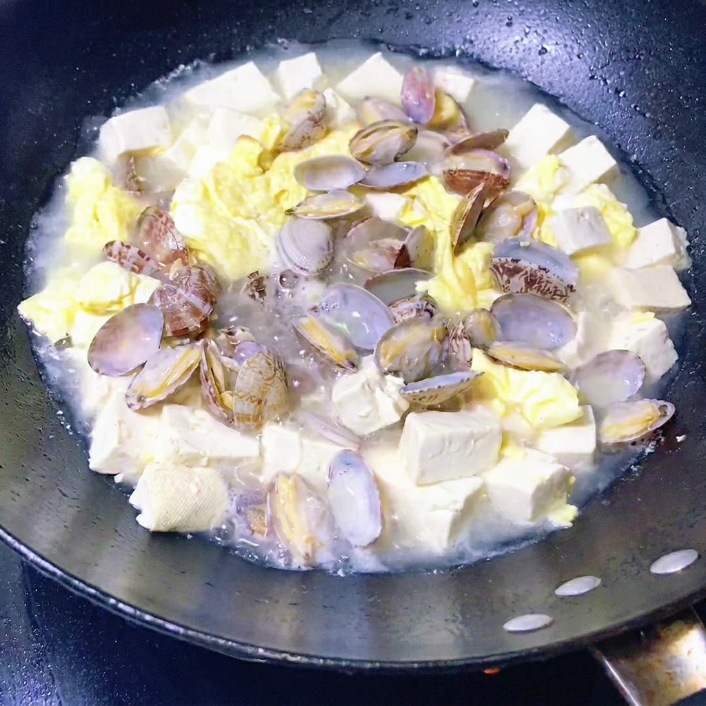 Blattgemüse wird in eine Pfanne mit Muschel-, Tofu- und Eiereintopf gegeben.