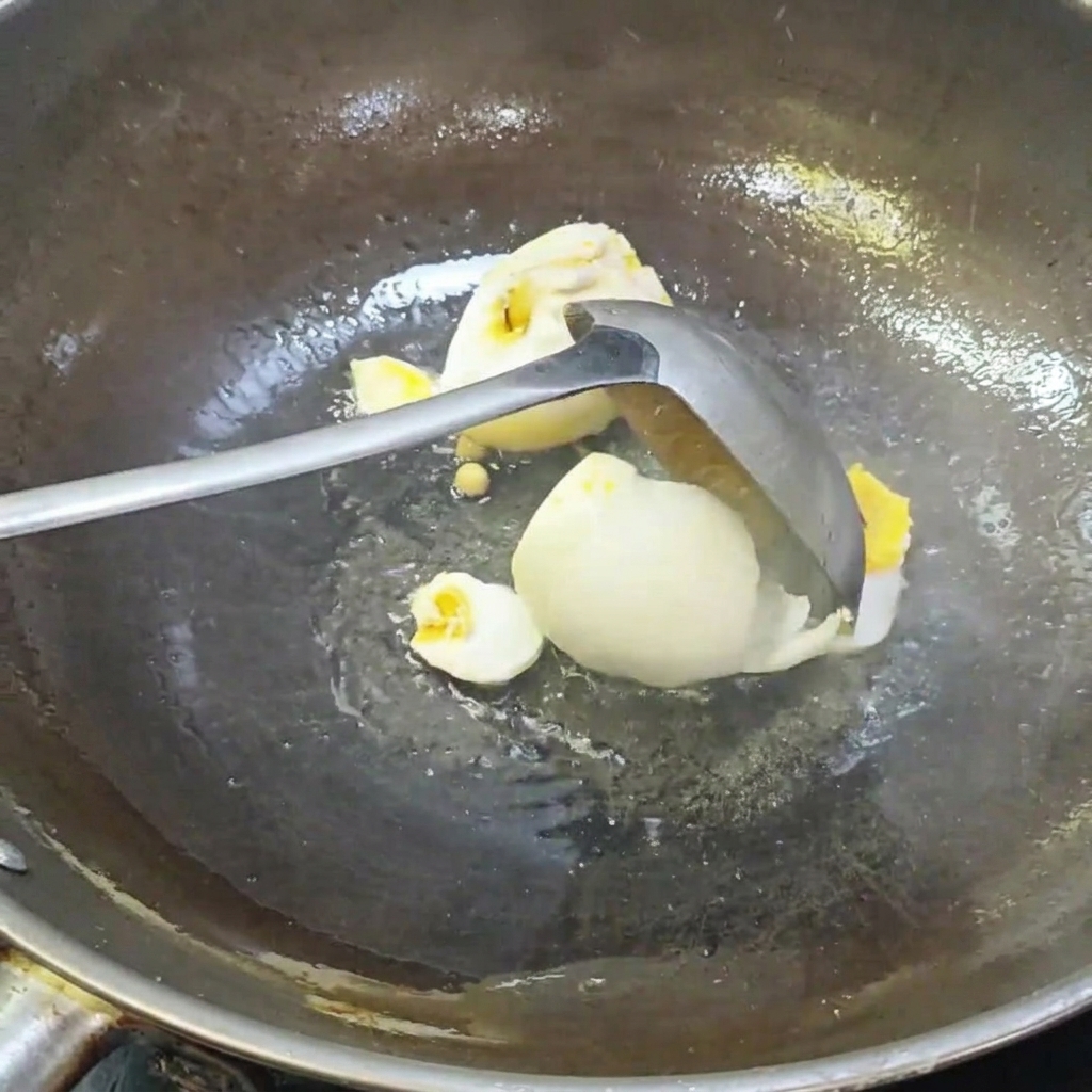 Ein Schöpflöffel zerteilt gesalzene Enteneier in einem Wok.