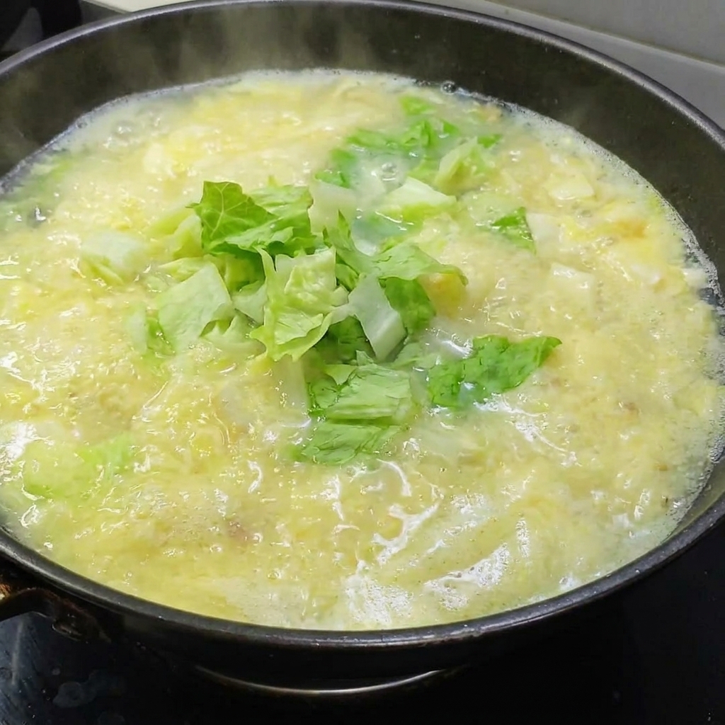 Frischer Salat wird in die köchelnde goldene Suppe gegeben.