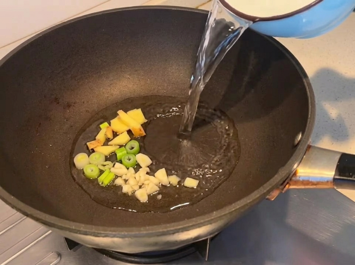 Wasser wird in eine Pfanne mit angebratenen Aromen gegossen.