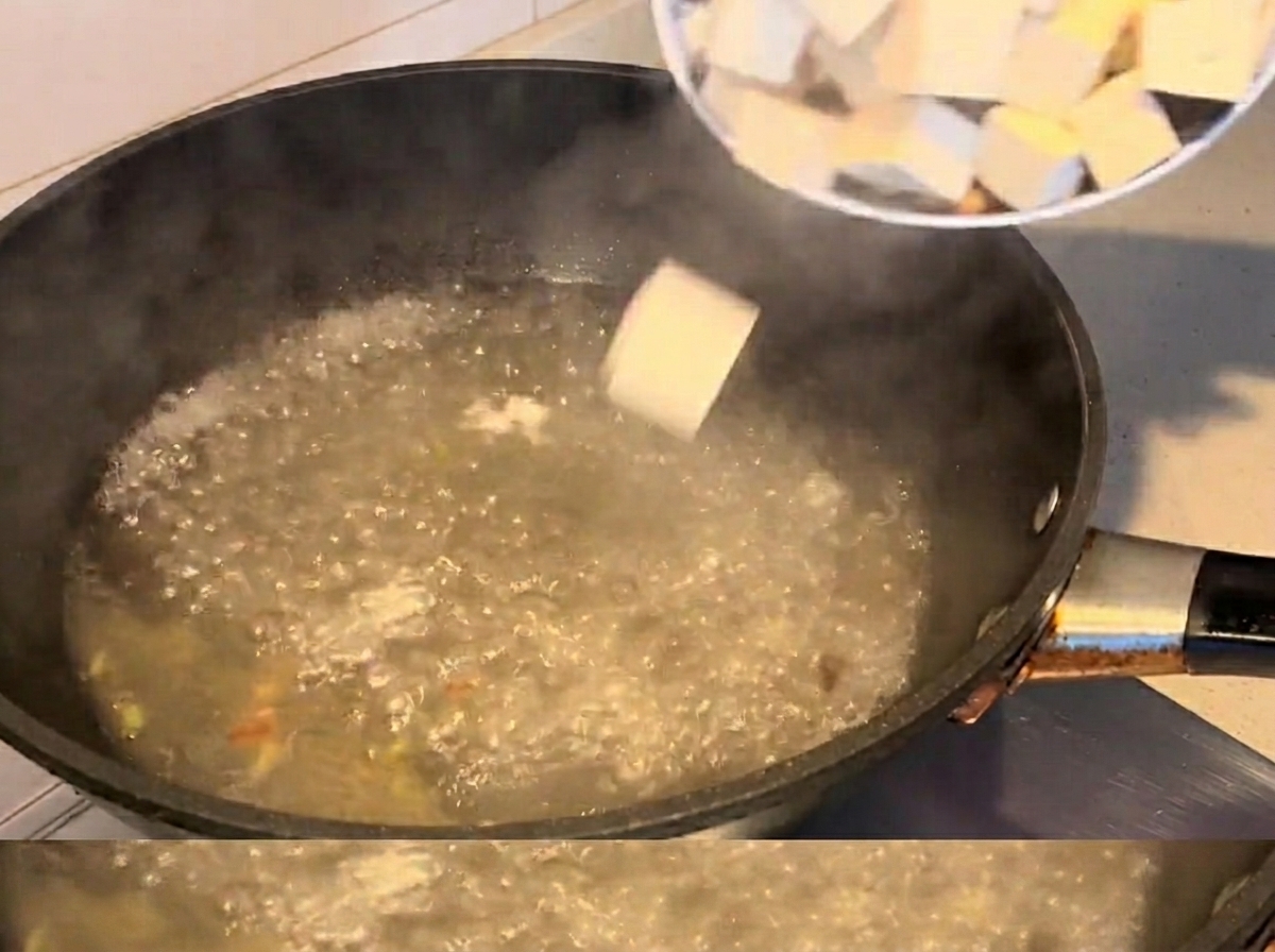 Tofuwürfel und Muscheln kochen in einer kochenden Suppe.
