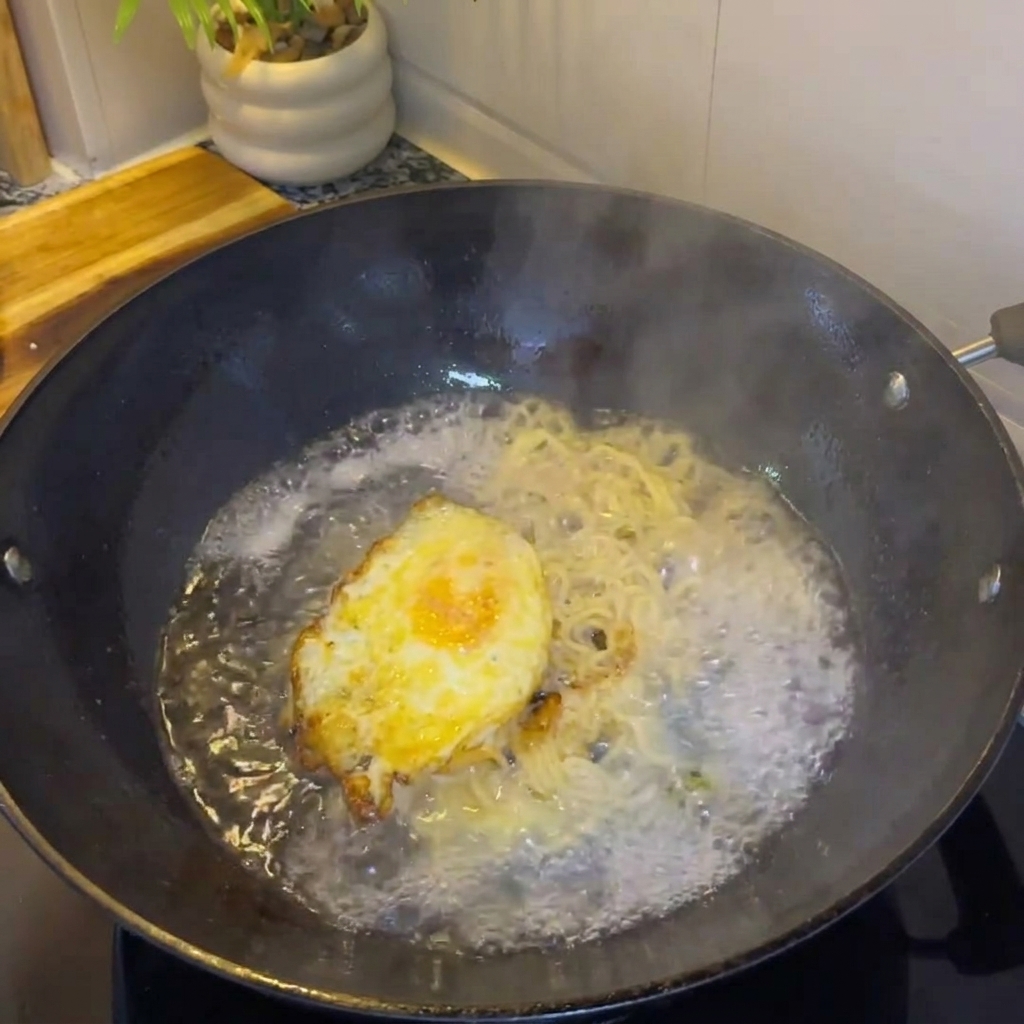 Heißes Wasser wird in den Wok zum Ei und den Zwiebeln gegossen, wodurch eine Brühe entsteht.