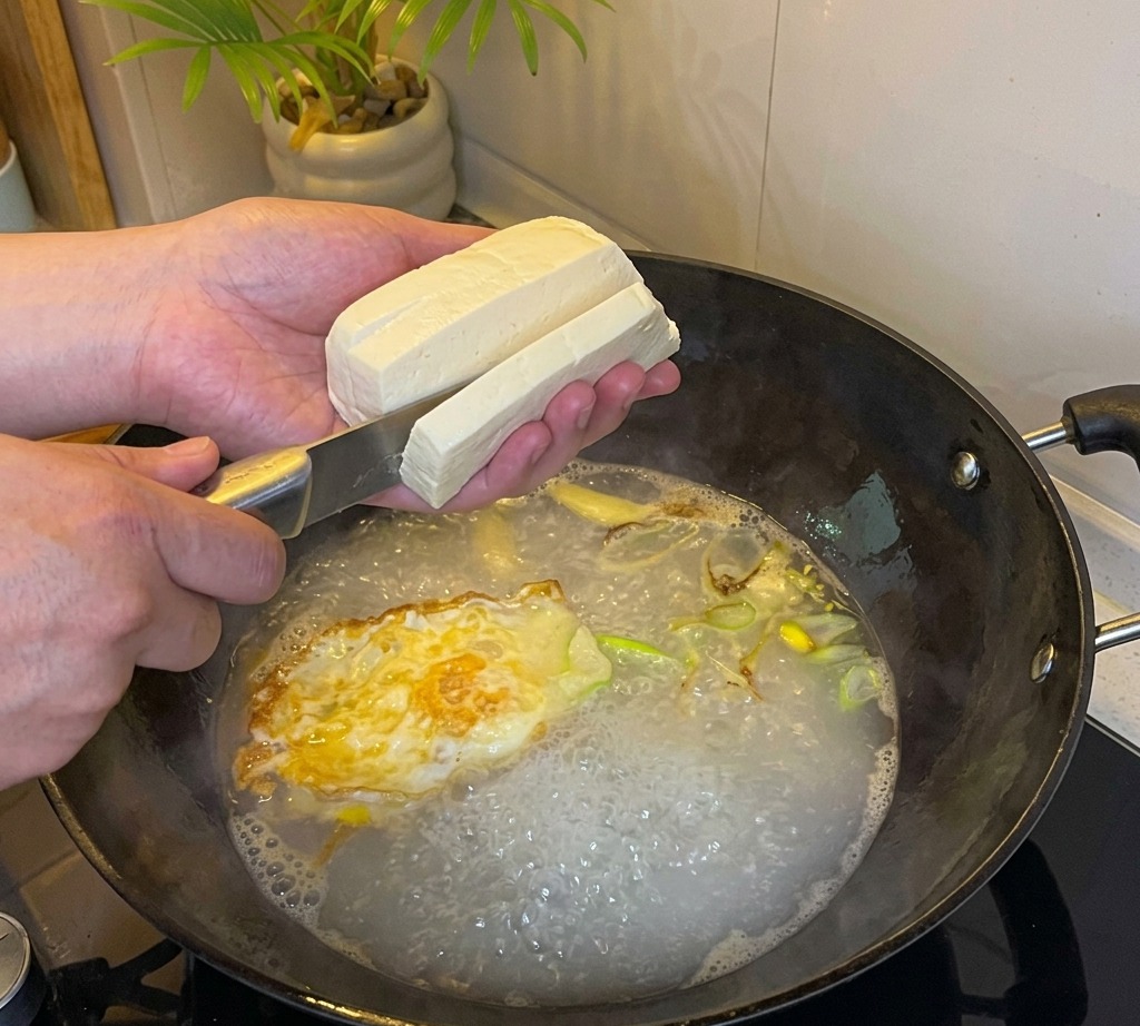Tofu wird direkt in die kochende Suppenbasis in Würfel geschnitten.