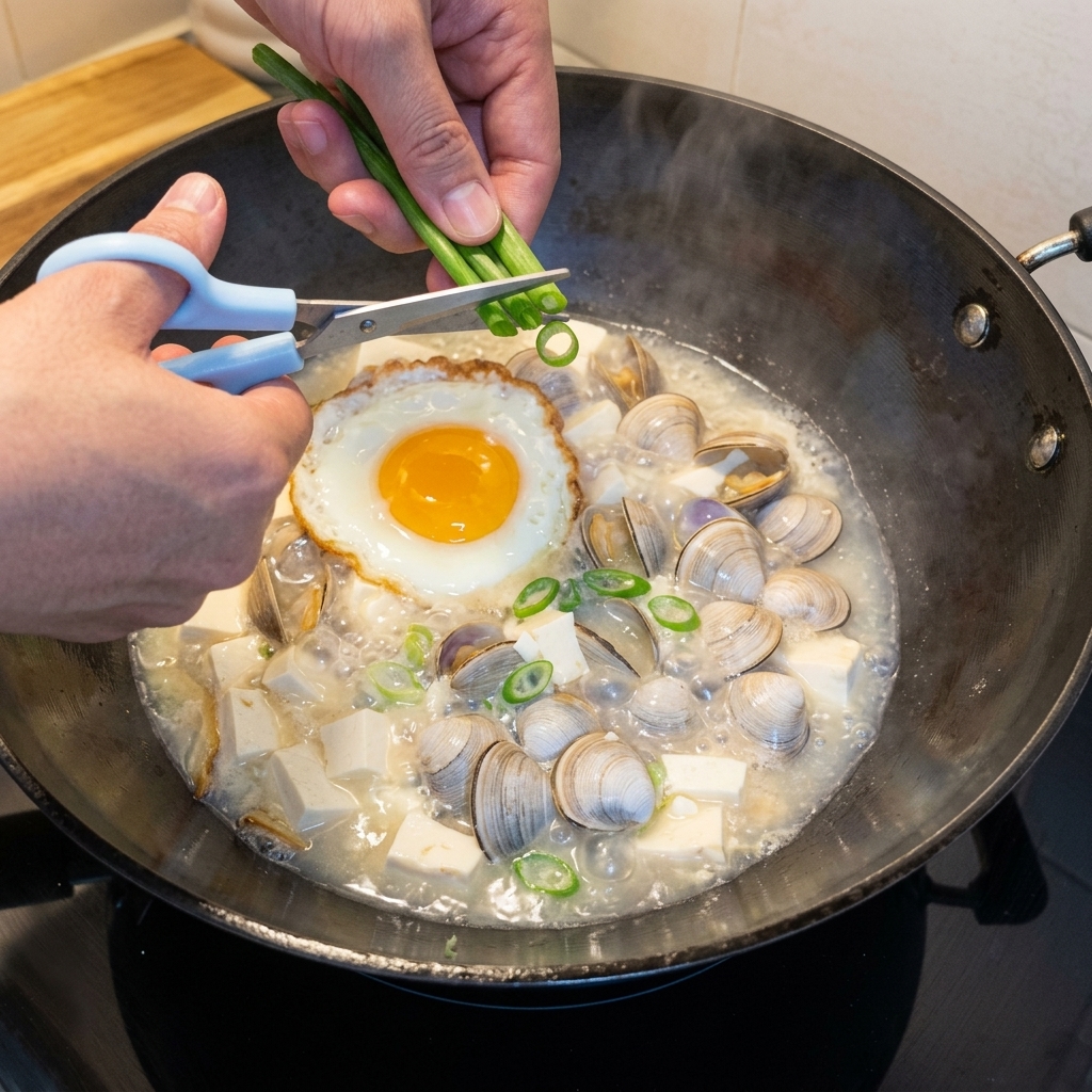 Frisch gehackte Frühlingszwiebeln werden über einen blubbernden Topf mit Tofu-Muschel-Suppe gestreut.