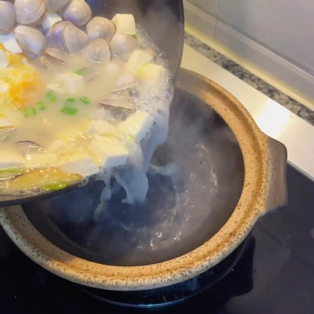 Tofu-Muschel-Suppe wird in einen rustikalen Serviertontopf gegossen.